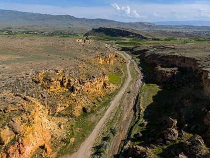 Narrow road leads through a rocky canyon with scattered green areas, aerial view, landscape at