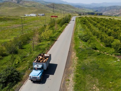 A lorry driving on a country road surrounded by green countryside, aerial view, lorry transporting