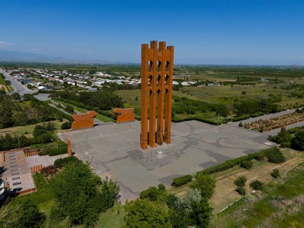 Large modern monument surrounded by landscape and small buildings under blue sky, aerial view,