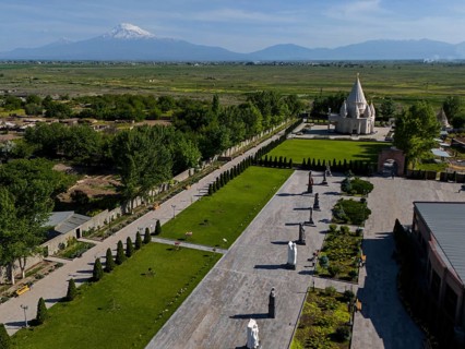 Spacious garden with statues and temple, surrounded by nature and mountains in the distance, aerial