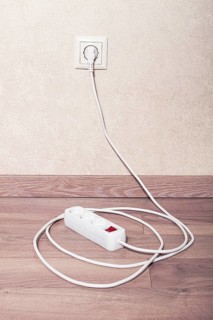 Electrical power strip connected to wall outlet on wooden floor in bright room