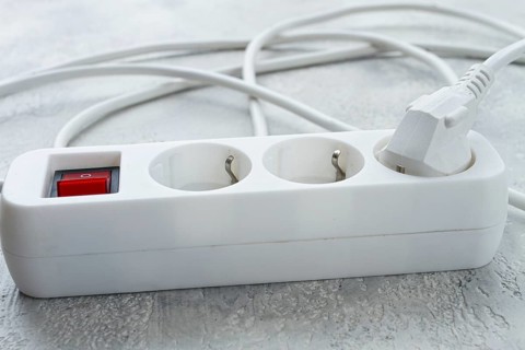 Power strip with multiple sockets and a switch in a cluttered setup on a textured surface during