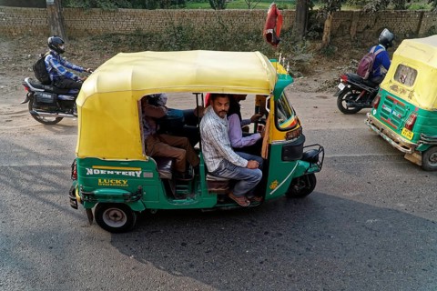 Yellow and green rickshaw with riders on a busy road, accompanied by motorcyclists, Agra, Jodhpur,