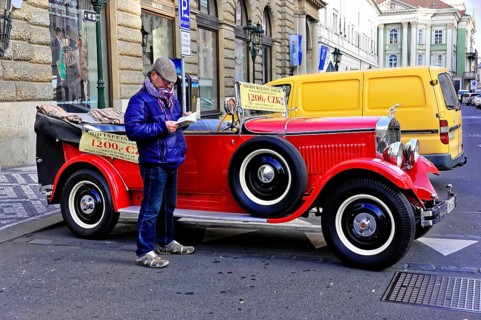Prague, Czech Republic, Europe, Man reading in front of a classic red vintage car on a busy street