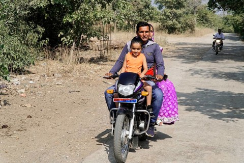 Kota, Rajasthan, North India, Asia, Family riding a motorbike along a rural road in sunny weather,