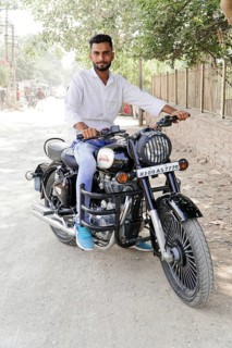 Kota, Rajasthan, North India, Asia, Man sitting on a black Royal Enfield motorbike on a dusty road,