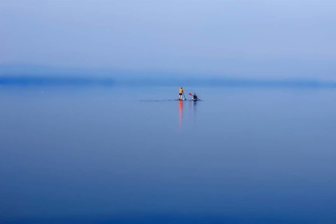 A calm lake (Steinhuder Meer) with paddleboarders under a blue and wide sky, Wunstorf