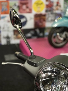 Mirror of a retro scooter in the foreground with colourful posters in the blurred background,