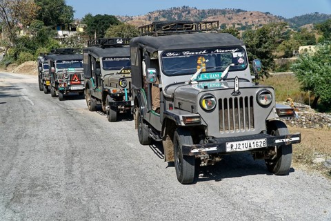 A convoy of jeeps drives along a country road in a mountainous region, Ranakpur, Jodhpur,