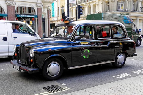 Black taxi driving on a busy London street in daylight, London, London region, England, United