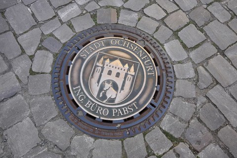 Round manhole cover with town coat of arms and inscription, paving stones, ground, Ochsenfurt,