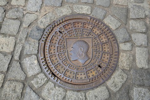 Round manhole cover with city coat of arms, inscription, cobblestones, floor, head, African,