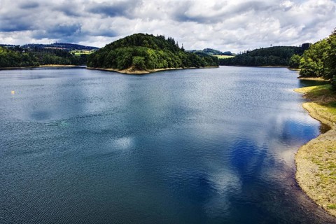 A calm lake (Aggertalsperre) with a wooded island, cloudy sky and reflecting water, Bergneustadt