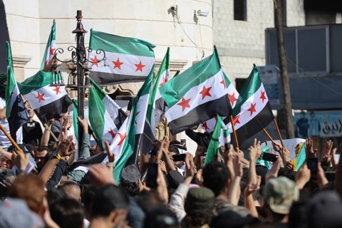 Thousands of Syrians march in Idlib carrying the Syrian revolutionary flag during a protest against