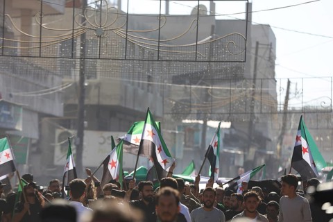 Thousands of Syrians march in Idlib carrying the Syrian revolutionary flag during a protest against