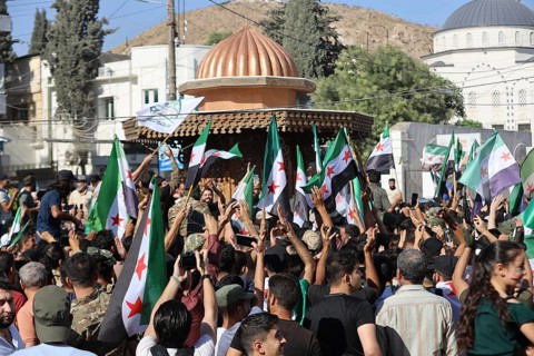 Thousands of Syrians march in Idlib carrying the Syrian revolutionary flag during a protest against