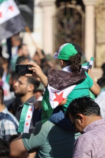 Thousands of Syrians march in Idlib carrying the Syrian revolutionary flag during a protest against