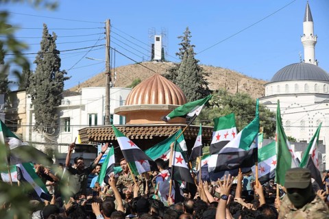 Thousands of Syrians march in Idlib carrying the Syrian revolutionary flag during a protest against