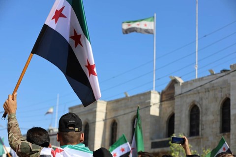 Thousands of Syrians march in Idlib carrying the Syrian revolutionary flag during a protest against