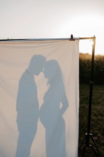 Pregnant young woman with partner in silhouette behind a sheet