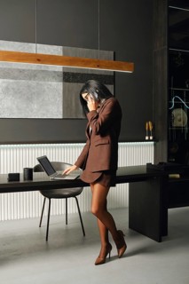 A businesswoman stands in a modern office space, engaged in a phone conversation while reviewing