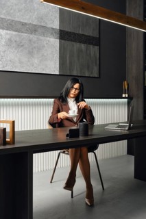 A woman in business attire sits at a sleek desk in a modern office, taking a cup of coffee. The