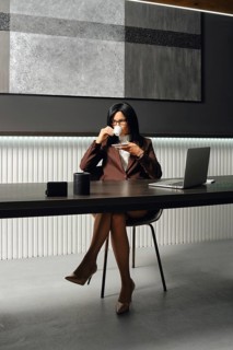 A confident businesswoman is seated at a sleek desk in a contemporary office. She sips coffee while