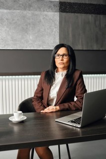 A focused businesswoman dressed in formal attire sits at a desk in a modern office environment. She