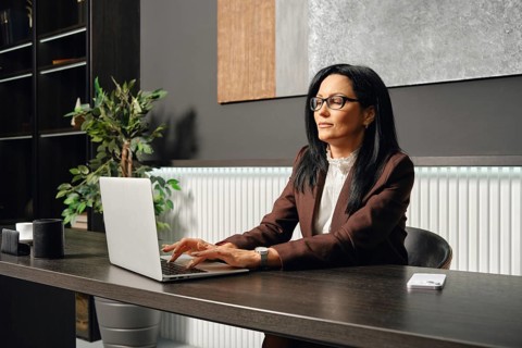 A businesswoman sits at a desk and typing on her laptop in an office. The space features elegant