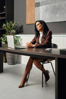 A woman dressed in business attire sits at an office desk in office and looking at the screen of