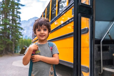 Happy elementary school student carrying backpack is waiting for the school bus in a mountain