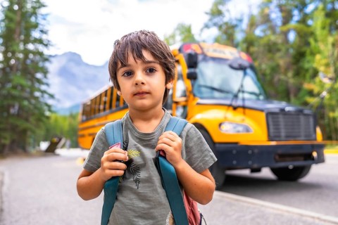 Elementary school student carrying backpack standing on a mountain road waiting for the school bus