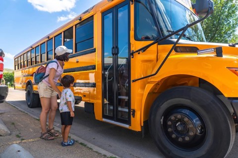 Caring mother supports her son as he prepares to board the school bus for his first day back to