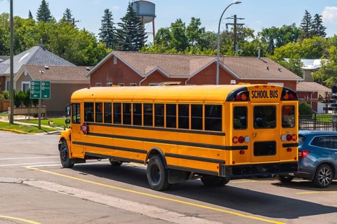 Yellow school bus driving down a suburban street during the daytime, transporting students to or