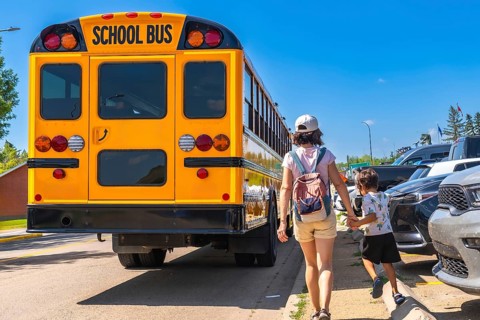 Mother holding son's hand walking towards a school bus on the first day back to school,