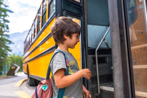 Preschool student entering a school bus, wearing a colorful backpack and beaming with excitement