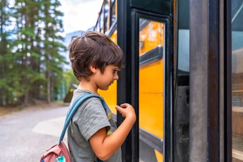 Curious preschool student with a backpack examines a yellow school bus before boarding, showing the