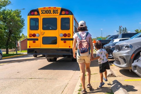Mother walking her son to the school bus on the first day back to school, holding hands and heading