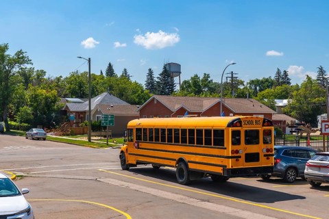 Classic yellow school bus driving away from an intersection in a quiet residential area, marking