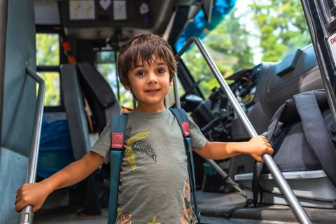 Happy preschool student entering a school bus, gripping the handrail with excitement, embracing the