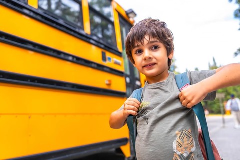 Elementary school student wearing a backpack, waiting for the bus on a bright, sunny day, excitedly