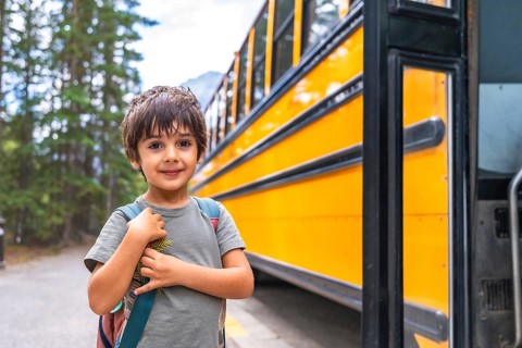 Elementary school student waiting at a mountain road, carrying a backpack and anticipating the