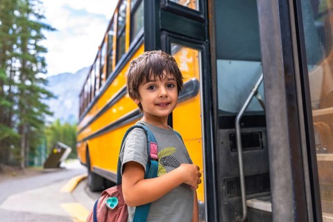 Preschool student with backpack embarking on a yellow school bus, excited for the new academic