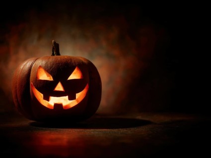 A spooky carved glowing pumpkin in a dark room, symbolising Halloween and autumnal mood, AI