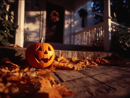 A carved pumpkin with a smiling face stands on a house wall in front of a residential building,