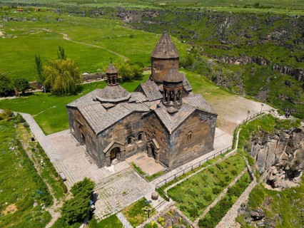 Medieval stone church with a surrounding green landscape and cliffs, aerial view, Saghmosavank