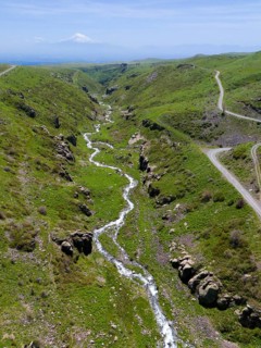 A panoramic view shows a river flowing through a green, hilly landscape, aerial view, river and