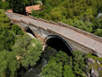 Stone bridge with arches over a river, surrounded by lush trees and nature, aerial view, Three-arch