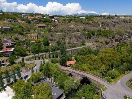 Idyllic village landscape amidst hills, near a river, with clear clouds in the sky, aerial view,