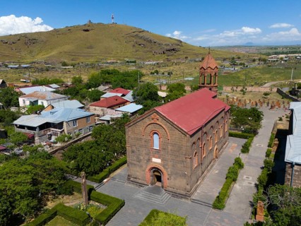 Small brick church in a rural setting with a nearby hill and blue sky, aerial view, Church of St